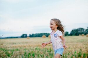 smiling girl running towards left on green field